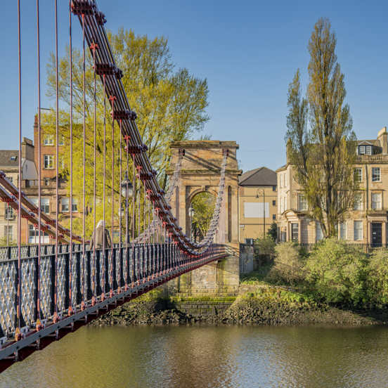 View across the River Clyde of a red metal South Portland Street Suspension Footbridge