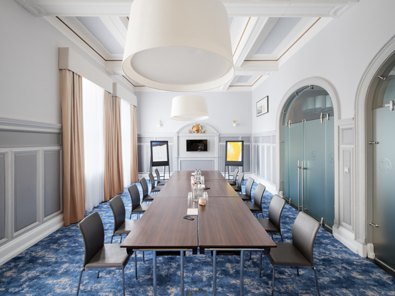 Boardroom meeting room set up in a heritage property with modern facilities. Wooden table surrounded by dark grey leather chairs. 