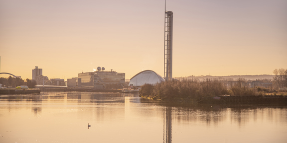 Dawn view across the River Clyde of the square, glass building of BBC Scotland, of the crescent-shaped glass front of the Glasgow Science Centre and of the tall metal spire of the Glasgow Tower