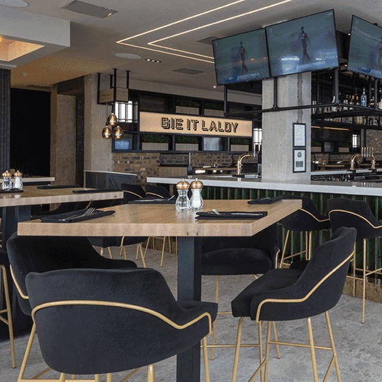 The Sandman Hotel's restaurant, Chop Grill & Bar. High stools line both sides of a well stocked, marble topped bar. Television screens booths and high tables are also visible.
