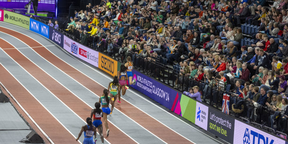 Busy seated crowd watch athletes run on the track.