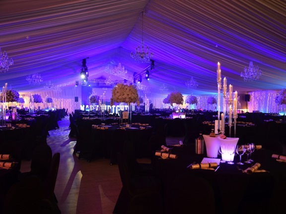 Marque set up for a dinner - round tables dressed with black tablecloths. White candles and flowers dress the table top.