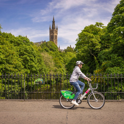 Cyclist, with tower of the Gothic revivals style spire of the University of Glasgow in the background, surrounded by greenery