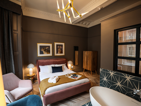 Luxurious hotel bedroom with king-size bed, free-standing bath and gold accents. 