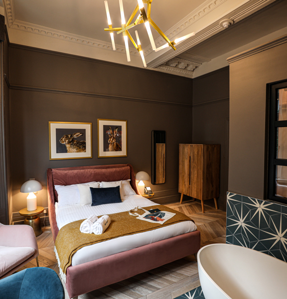 Luxurious hotel bedroom with king-size bed, free-standing bath and gold accents. 