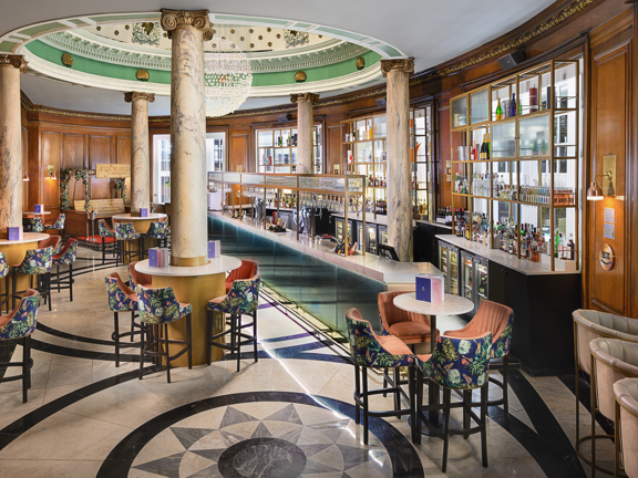 Heritage bar in voco Grand Central Hotel - marble flooring,  wood panelling, glass and golden mental gantry, occasional seating, bar stools with floral velvet coverings, marble pillars and giant crystal chandelier.  