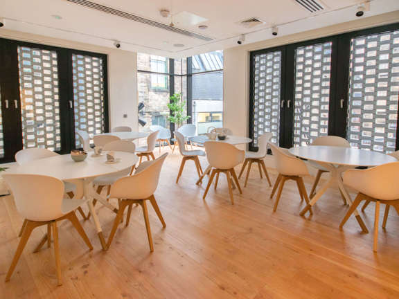 Light modern meeting room with pale wooden flooring, white table and chairs and floor to ceiling windows with black shutters. 