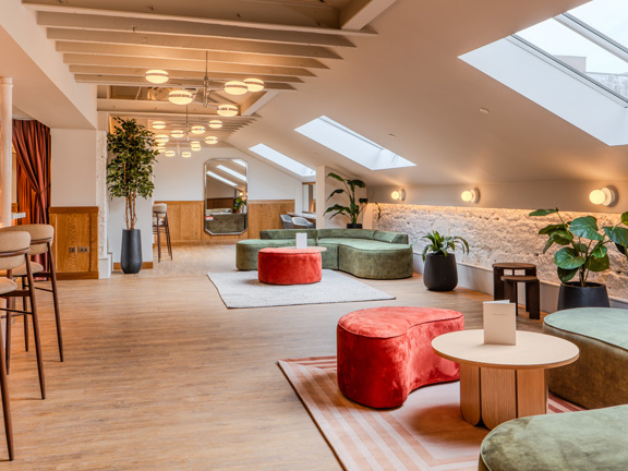 Large room with easy velvet sofas and stools in olive green and rust orange colours. Bar with high stools to the left.