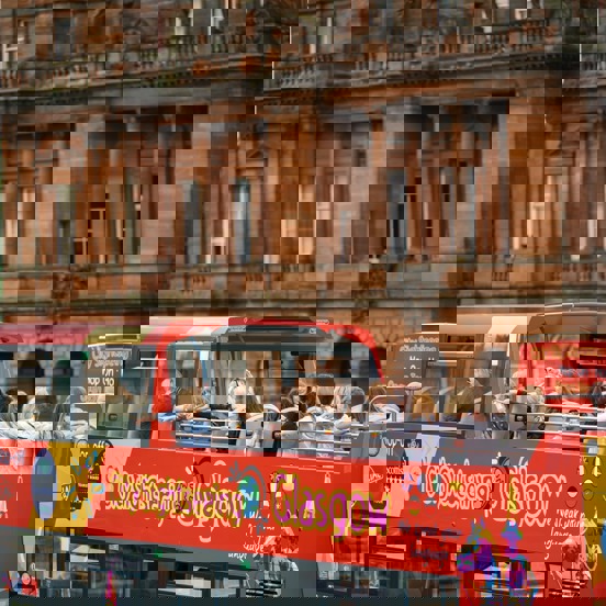 Glasgow City Sightseeing red open-top bus passing a red sandstone building.