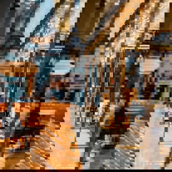 Marble topped bar with brass metal framework above and beige leather barstools lined up along one edge.