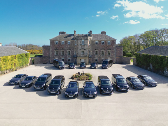 Fleet of black cars and peoples carriers outside a stately home