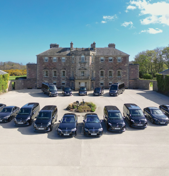 Fleet of black cars and peoples carriers outside a stately home