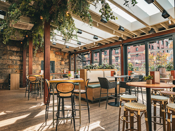 Interior of Kong bar in Glasgow featuring a cosy, modern space with wooden tables and stools, bi-folding doors and hanging greenery.