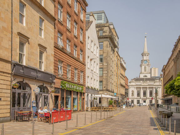 sunny city scene with people dining outdoors and spired building at the end of the street