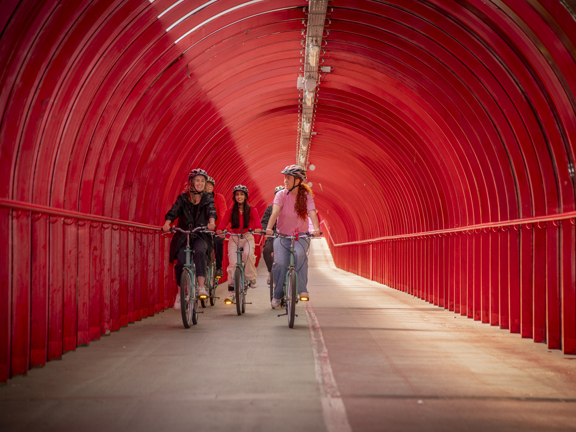 Five people cycle through covered red walkway in Glasgow.