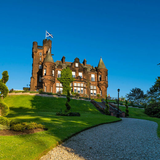 Baronial castle style building on top of a hilly landscaped garden