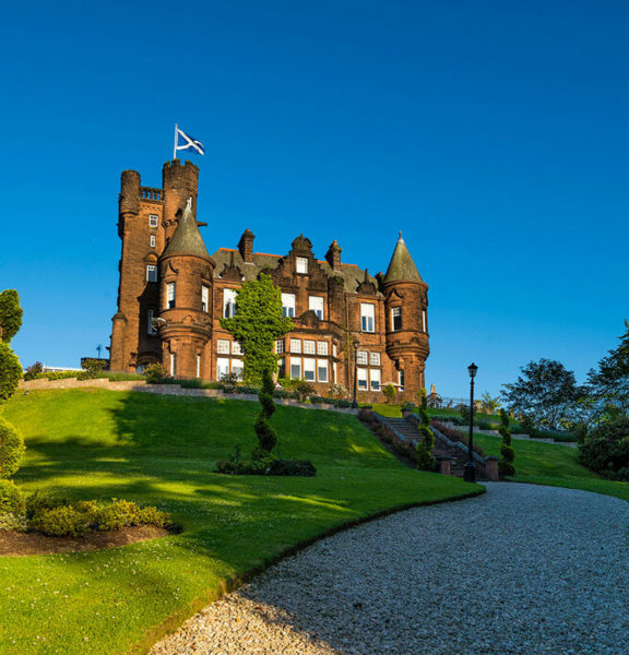 Baronial castle style building on top of a hilly landscaped garden