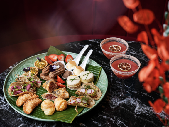 Plate of various canapes and two pink cocktails with slices of dried lemon on top. 