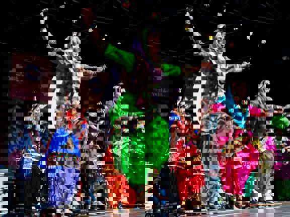 A group of women dancers in traditional clothing dance on stage in the sunshine at Glasgow Mela.