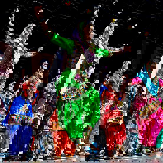 A group of women dancers in traditional clothing dance on stage in the sunshine at Glasgow Mela.