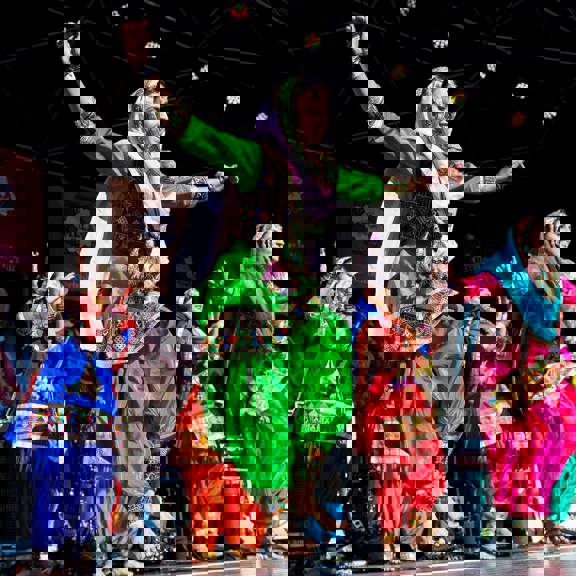 A group of women dancers in traditional clothing dance on stage in the sunshine at Glasgow Mela.