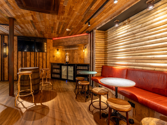 Small event space with various tables and chairs, wooden clad walls and a small bar at one end. 