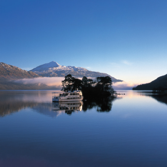 Boat on blue Loch Lomond with snowy hill in the background
