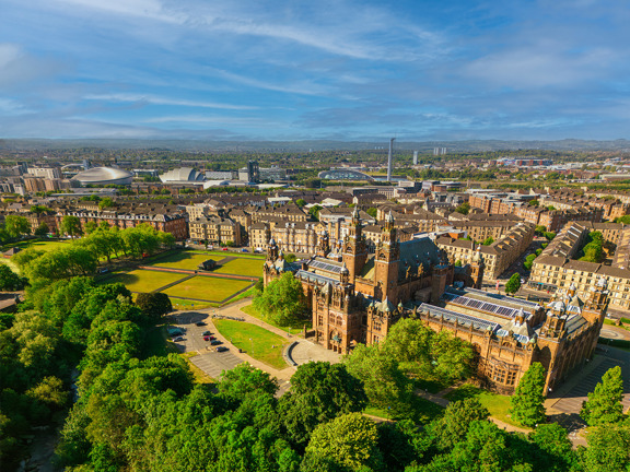Glasgow cityscape, with the Baroque-style Kelvingrove Art Gallery and Museum, surrounded by greenery. The modern buildings of the Scottish Event Campus and the Glasgow Science Centre are visible in the background