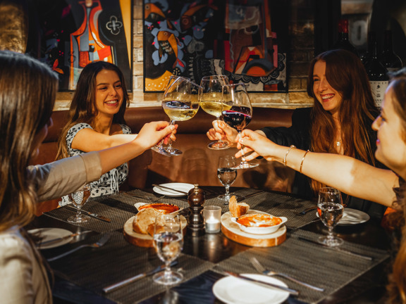 Four people sitting at a dining table 'cheersing' and awaiting food. 