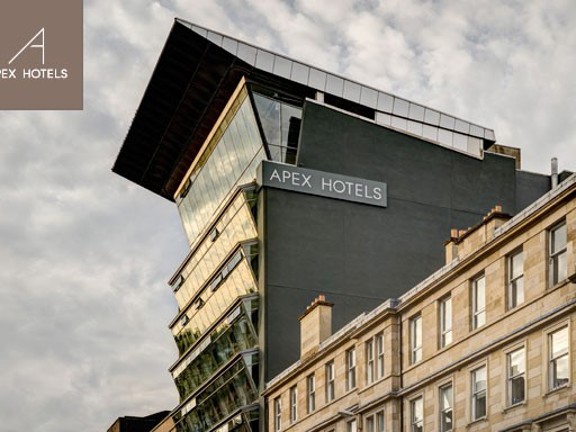 An external shot of the Apex Hotel. An angular grey modern building with many windows against a cloudy sky.