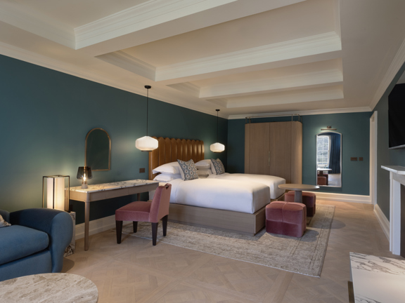 Hotel bedroom - large double bed with white linen sheets, fireplace, sofa, dressing table soft lighting and marble coffee table.