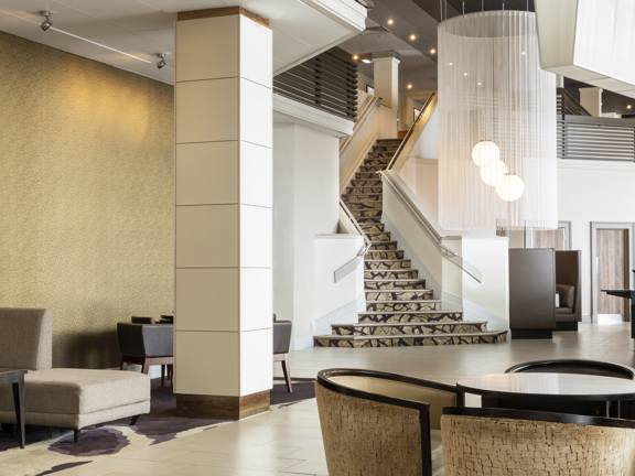 Hotel lobby with various chairs and tables.  Statement chandelier hangs in middle of room. 