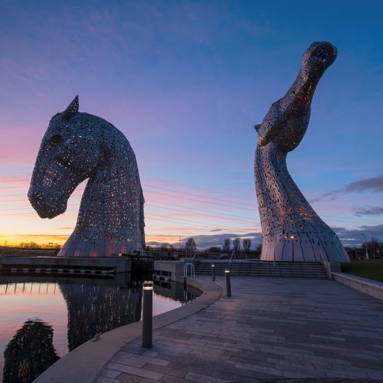 Two giant metal kelpie head sculptures at dusk
