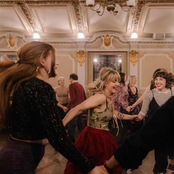 Visitors taking part in a ceilidh dance in an ornate historic venue in Glasgow
