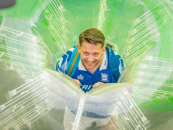 man smiling and peering out of a giant inflatable football.