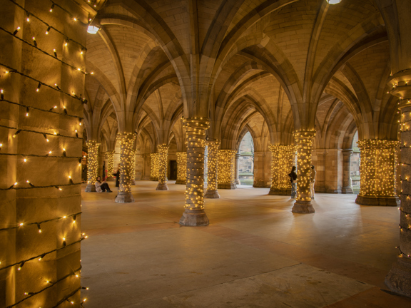 Gothic-revival-style arches and columns of University of Glasgow Cloisters, with fairy lights wrapped around each column.