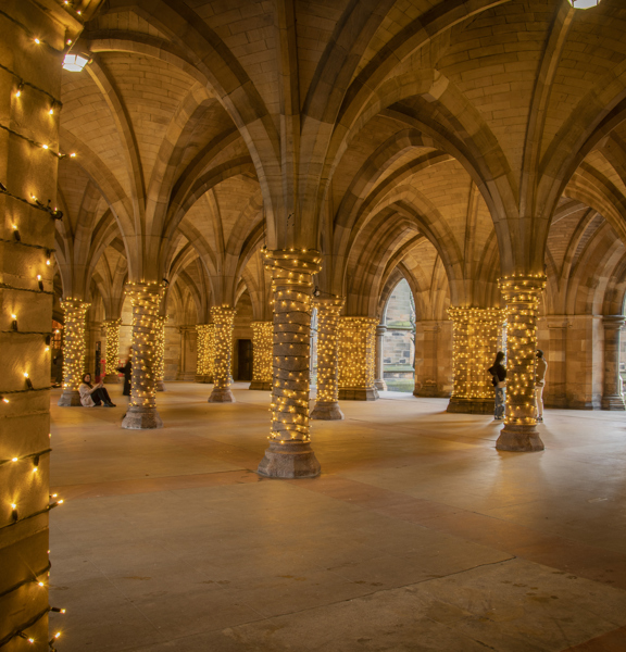Gothic-revival-style arches and columns of University of Glasgow Cloisters, with fairy lights wrapped around each column.