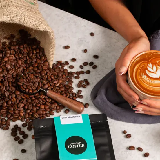 artistic display of coffee beans, a sachet of coffee reading Gordon St coffee and a hand holding a large mug of coffee