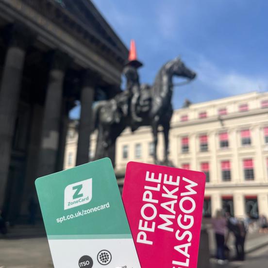 Person holding travel ticket, with Glasgow street scene in the background with Duke of Wellington statue