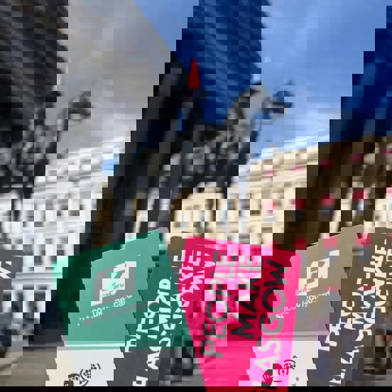 Person holding travel ticket, with Glasgow street scene in the background with Duke of Wellington statue