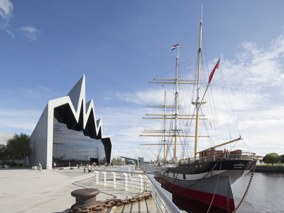 Sunny view of the modern, glass-fronted Riverside Museum, where the roofline reminiscent of a heartbeat on a monitor, with a three-masted 19th century Glenlee tallship docked outside.
