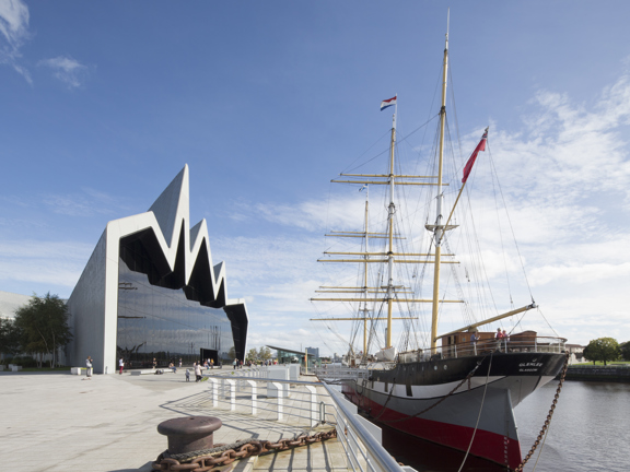 Sunny view of the modern, glass-fronted Riverside Museum, where the roofline reminiscent of a heartbeat on a monitor, with a three-masted 19th century Glenlee tallship docked outside.