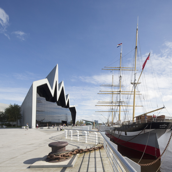 Sunny view of the modern, glass-fronted Riverside Museum, where the roofline reminiscent of a heartbeat on a monitor, with a three-masted 19th century Glenlee tallship docked outside.