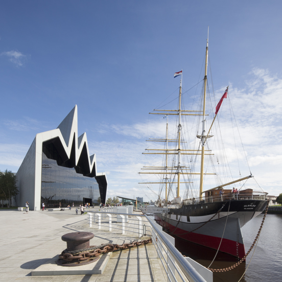 Sunny view of the modern, glass-fronted Riverside Museum, where the roofline reminiscent of a heartbeat on a monitor, with a three-masted 19th century Glenlee tallship docked outside.