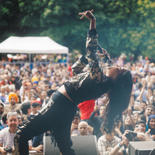 An artist on stage at Mela tipping her head backwards as the audience looks on
