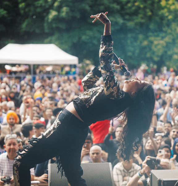 An artist on stage at Mela tipping her head backwards as the audience looks on