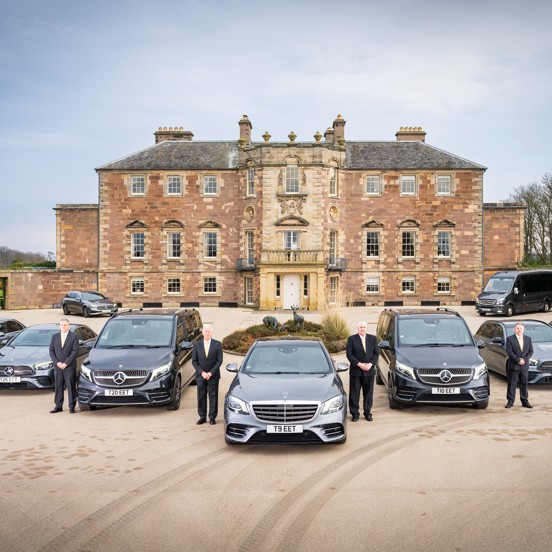 Fleet of silver Mercedes vehicles in front of a large blonde stone castle