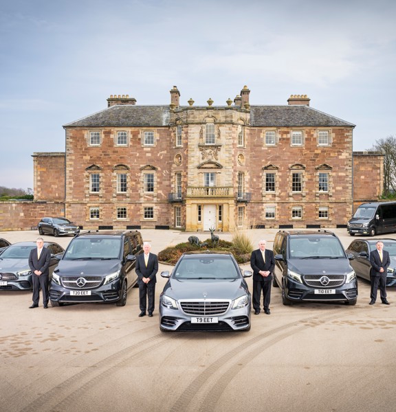 Fleet of silver Mercedes vehicles in front of a large blonde stone castle