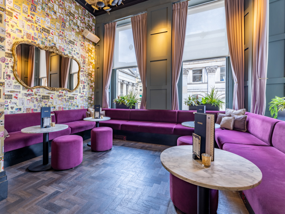 Intimate private event space with purple velvet sofas, marble tables, panelled walls and large windows.