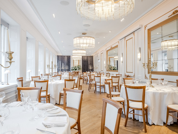 Large light room set for a dinner - all white walls with large mirrors and chandeliers hanging from the ceiling.